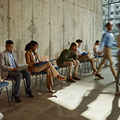 people waiting for interviews ; some are working on laptops and some look depressed